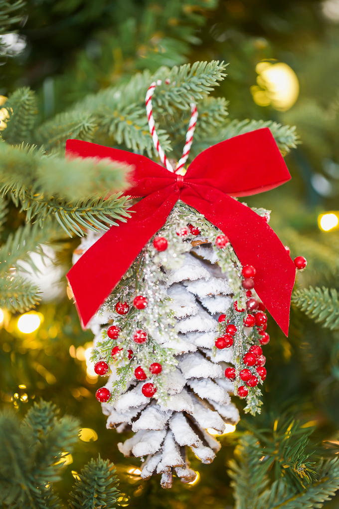 Snow covered pine cone ornament decorated with Christmas greenery and red berries