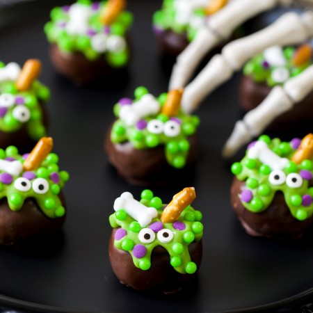 chocolate covered Halloween Cauldron OREO balls decorated with green chocolate, candy eyes, bones, and a pretzel stick