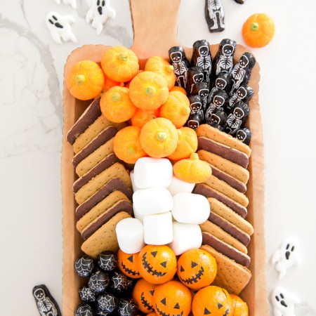 S'mores board ideas for Halloween with pumpkin marshmallows, pumpkin chocolate balls, and skeleton chocolate bars