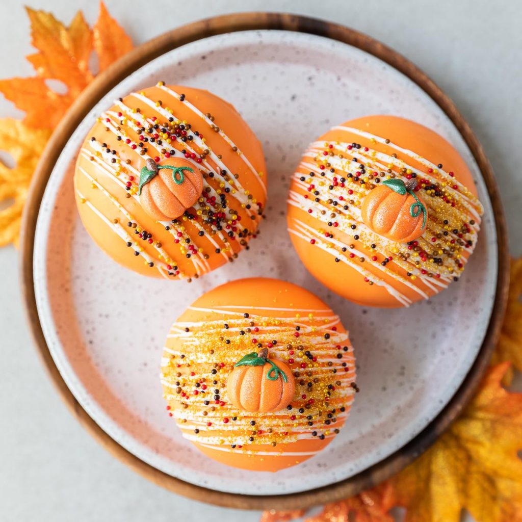 Easy pumpkin spice hot cocoa bombs in an orange chocolate shell with sprinkles