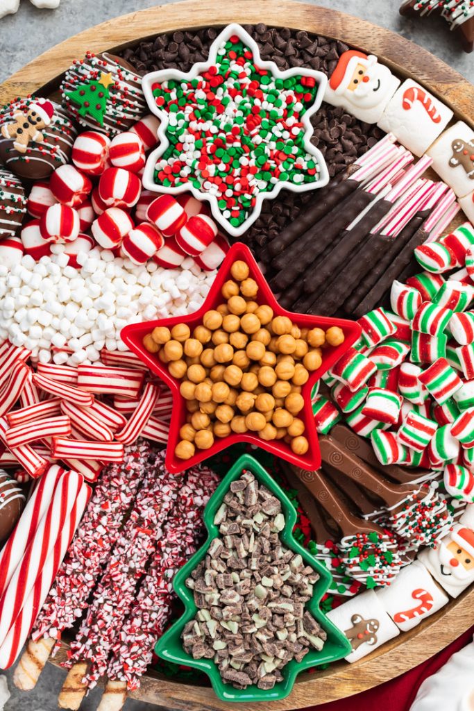 Holiday sprinkles, caramel bits, and peppermints in Christmas dishes for hot cocoa board tray