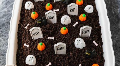 Halloween chocolate cake decorated with tombstones, ghosts, black cats, and pumpkins